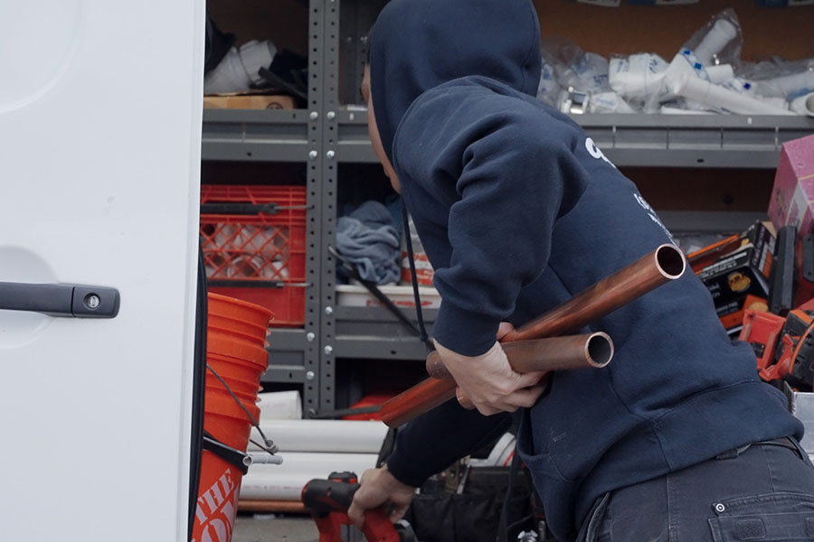Plumber retrieving copper pipes and tools from a service van