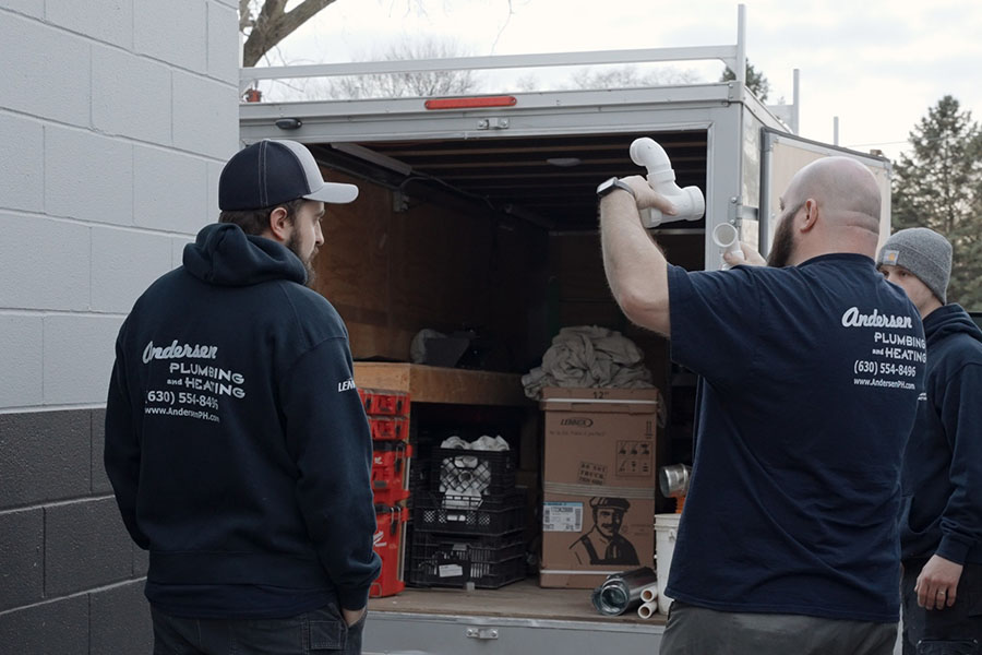 Team members unloading supplies from a plumbing service trailer while inspecting pipe fittings