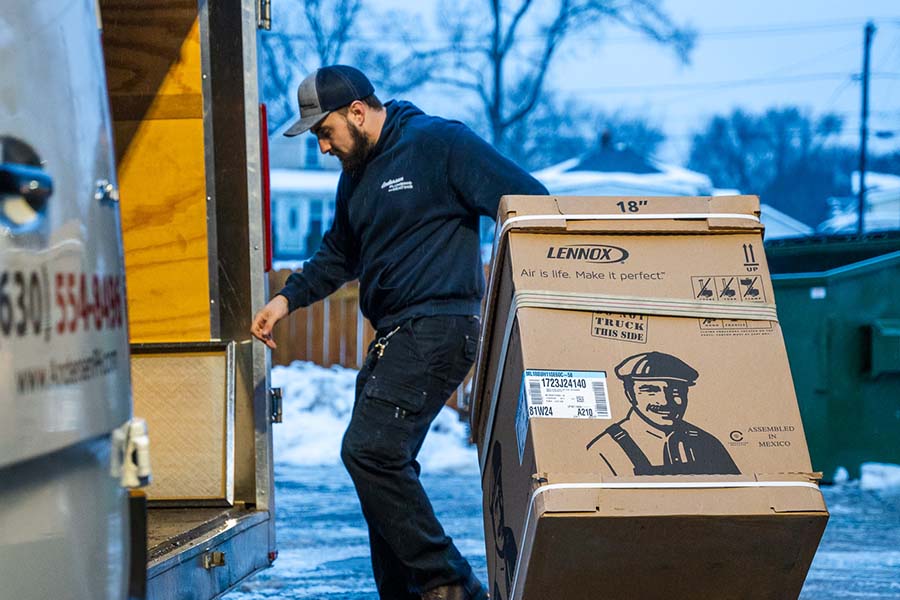 A man wearing a hoodie and cap moving an HVAC unit box from a trailer