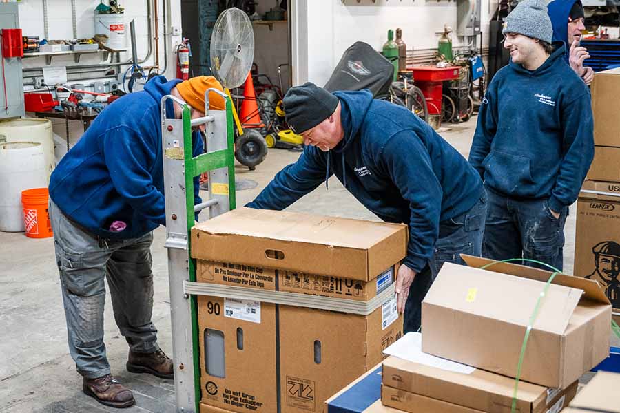 Workers in a warehouse unloading and handling HVAC equipment boxes