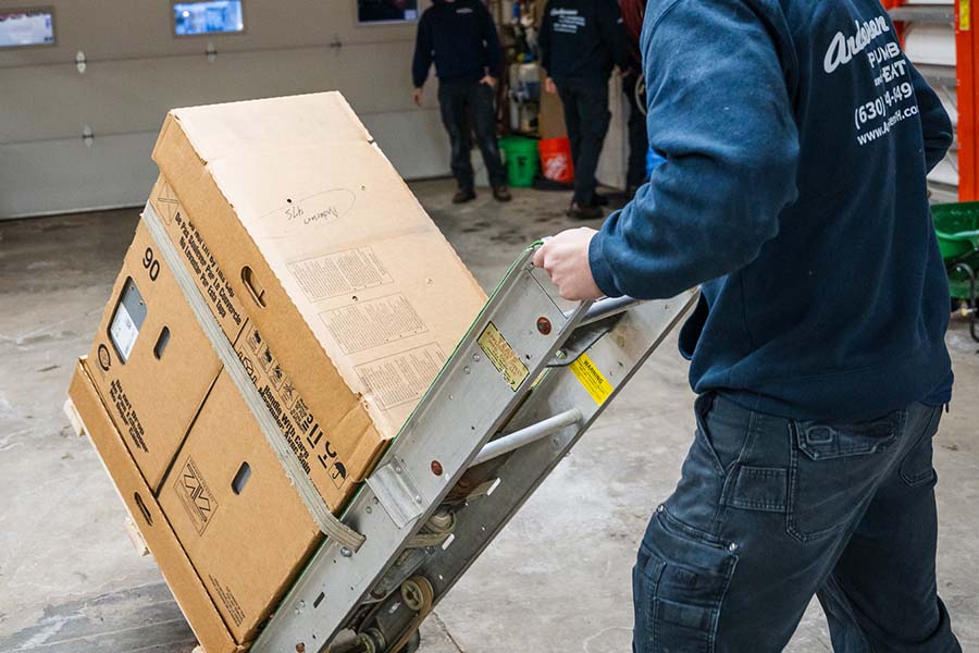 A worker using a dolly to move a large HVAC equipment box in a garage