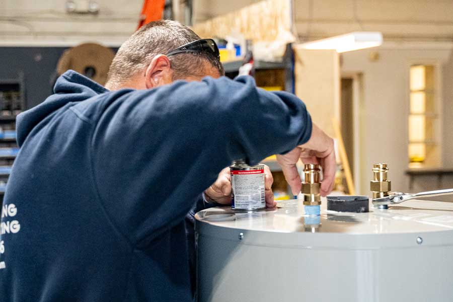 Technician installing fittings on a water heater in a workshop