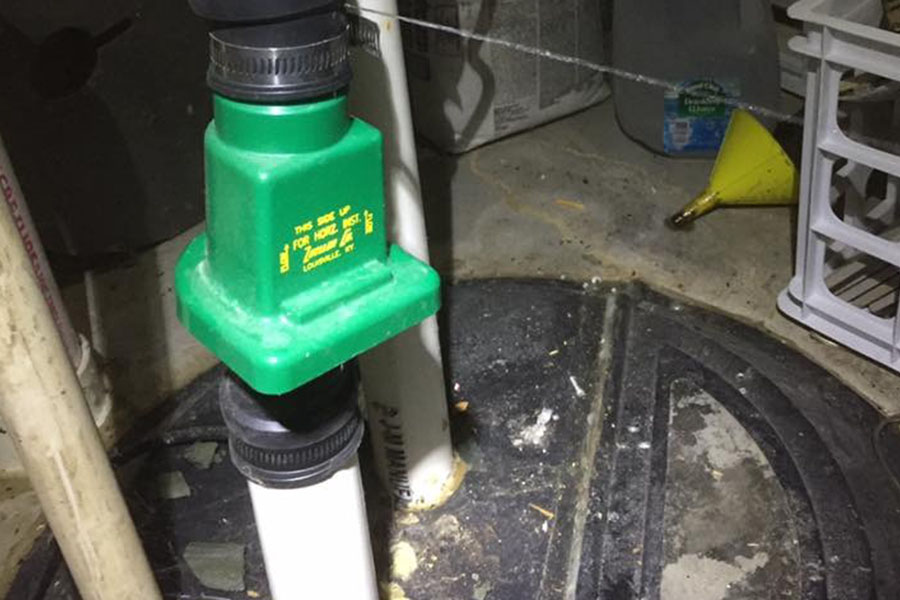Close-up of a sump pump system with a green check valve installed on a PVC pipe.