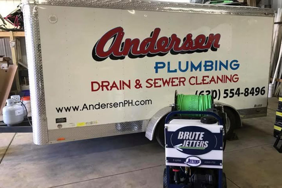 A branded Andersen Plumbing service trailer parked inside a workshop with drain cleaning equipment