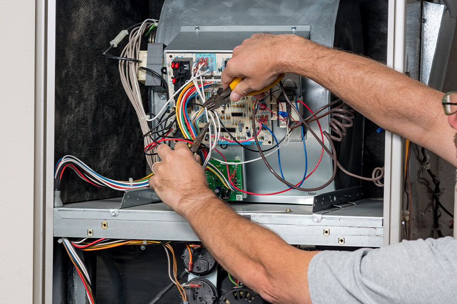 HVAC professional working on a circuit board and wiring inside a heating system