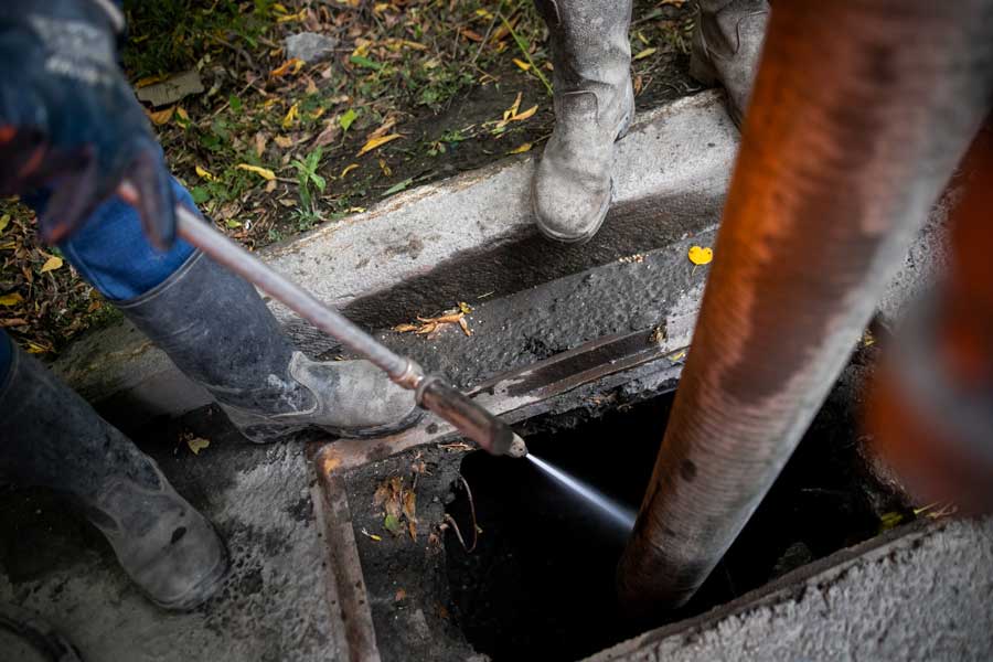 Workers using a high-pressure hose to clean a sewer drain