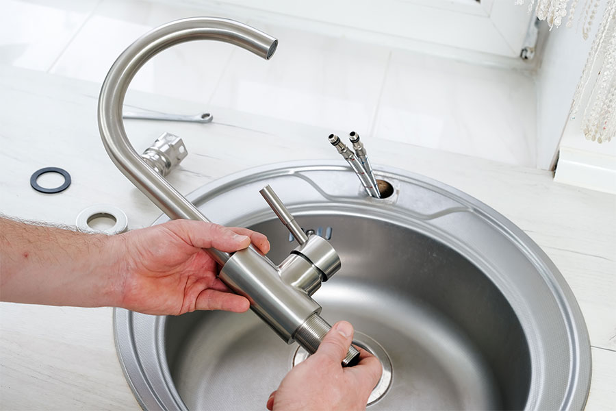Hands holding a silver faucet during a sink replacement.