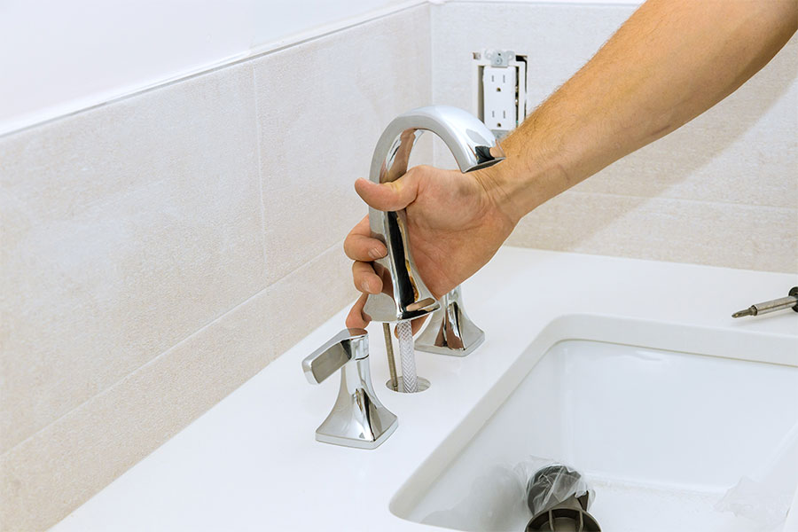 Plumber fitting a modern faucet on a white countertop