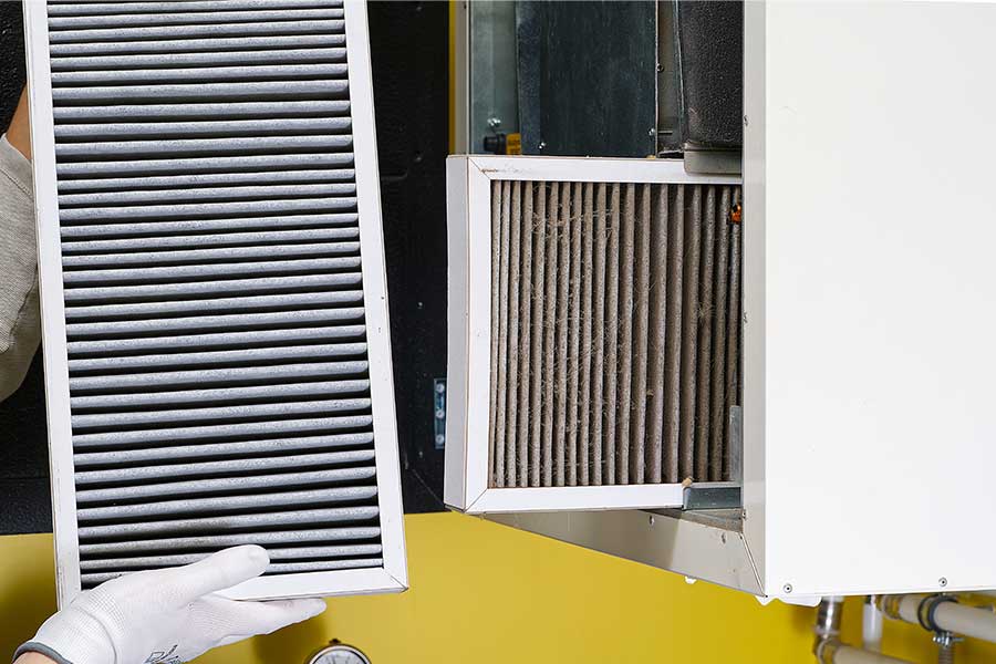 Hands with gloves holding a dirty HVAC air filter next to the unit