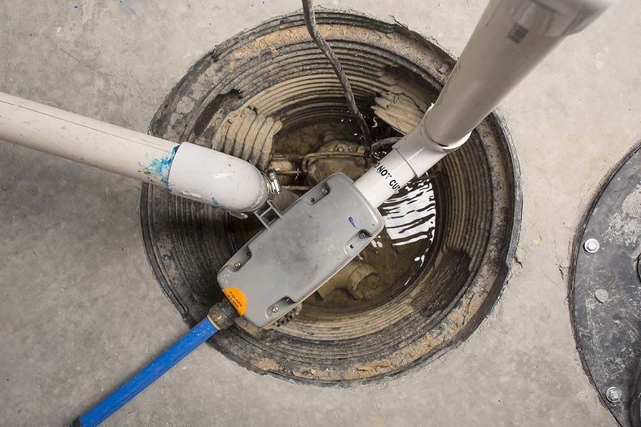 An open sump pump pit with connected PVC pipes and a backup pump system