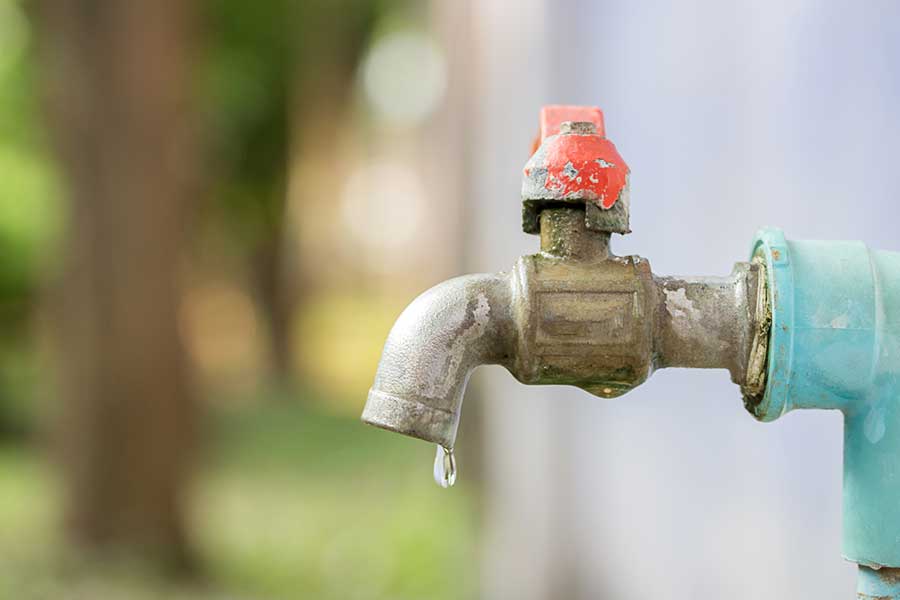 Old outdoor faucet with a red handle dripping water