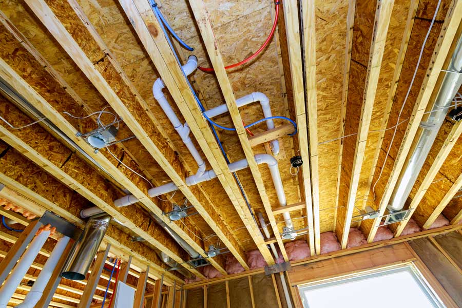 Exposed ceiling framing with plumbing, electrical, and HVAC ducts in a new home.
