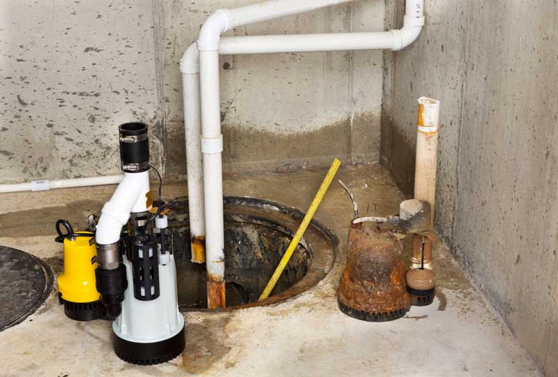 Basement sump pump installation with PVC drainage pipes.