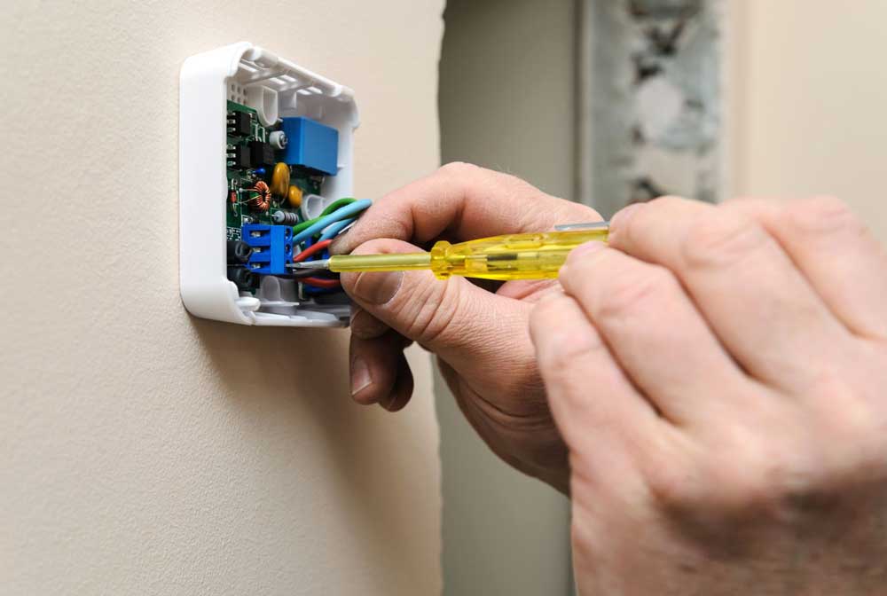 Technician installing a wall-mounted thermostat with a screwdriver