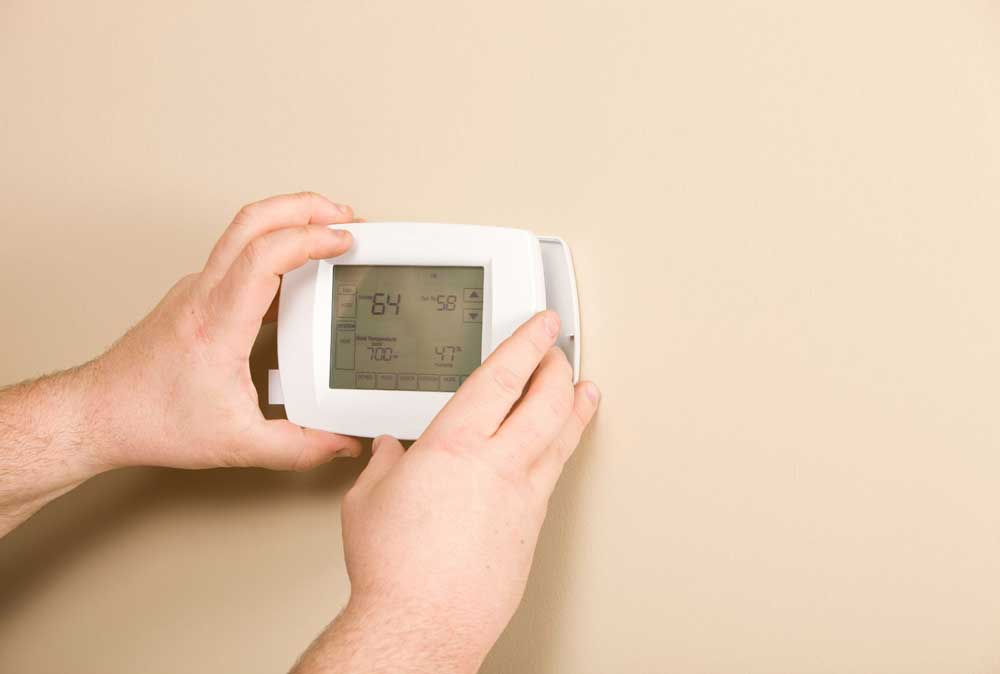 Hands installing or programming a wall-mounted thermostat
