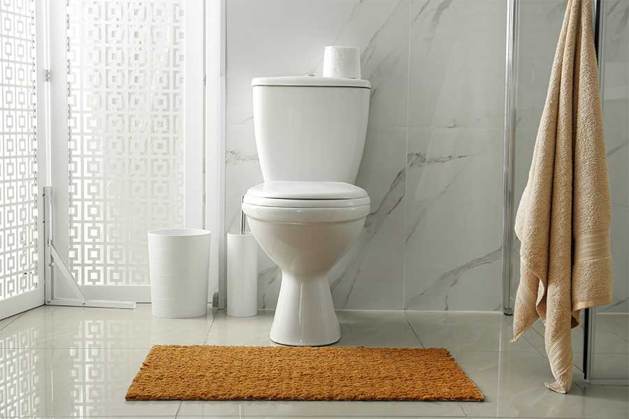 White toilet in a modern bathroom with marble walls and a brown rug