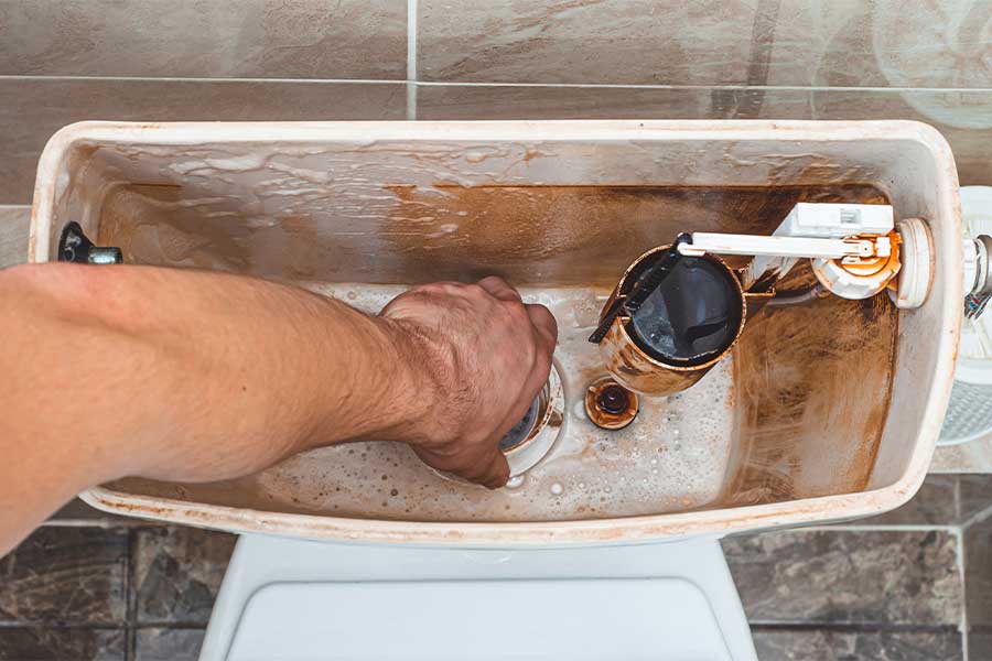Hand repairing a dirty toilet tank with rust and buildup