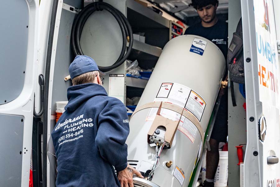 Two plumbers unloading a water heater from a service van.