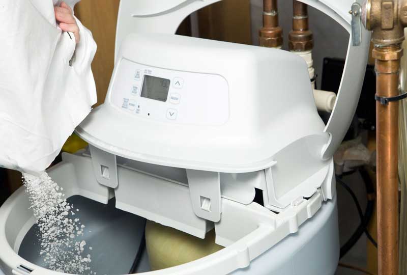 Person pouring salt pellets into a water softener system.