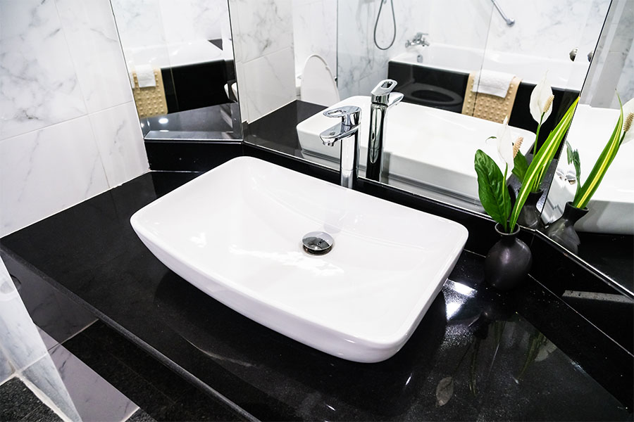 White bathroom vessel sink installation with chrome faucet on black countertop
